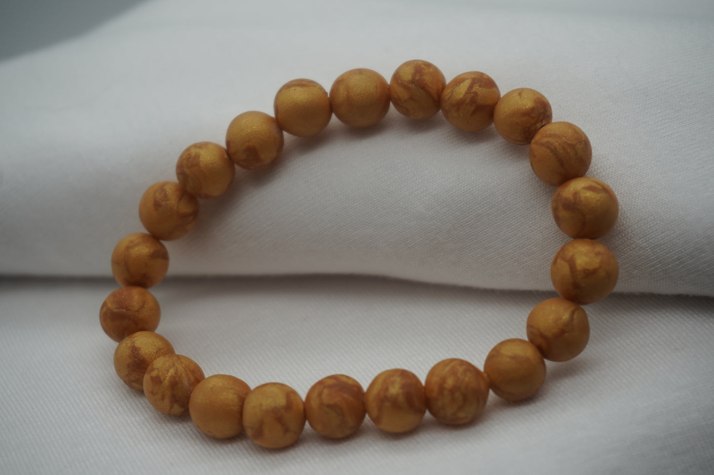 A bracelet made of yellow gold-colored round beads against a white backdrop.  The beads sparkle and have a slight swirled pattern.