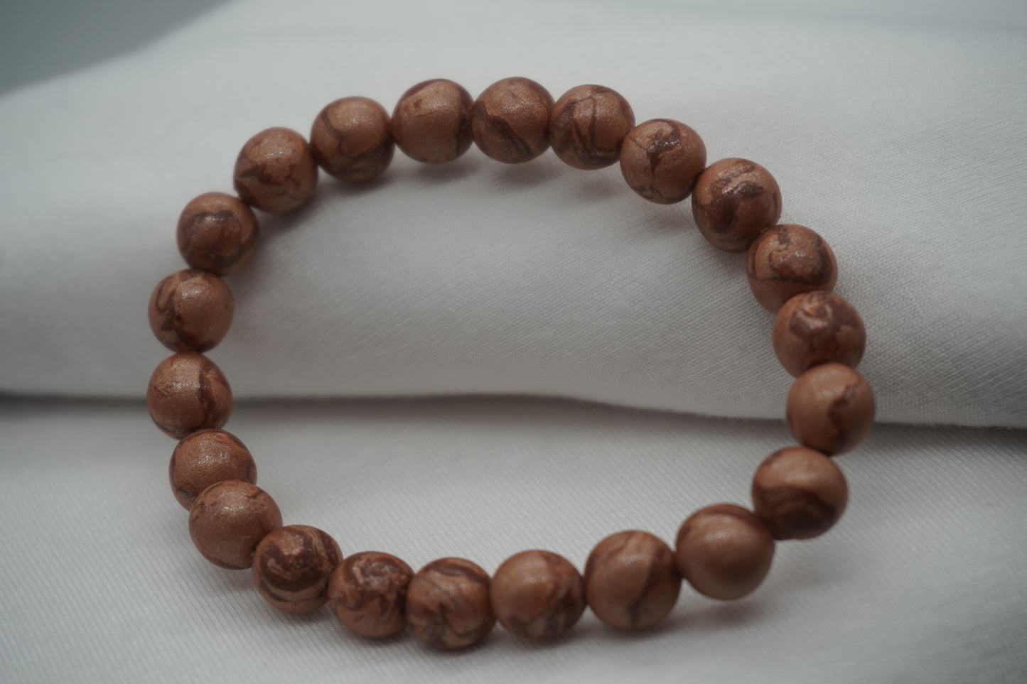 A bracelet made of copper-colored round beads against a white backdrop.  The beads sparkle and have a slight swirled pattern.
