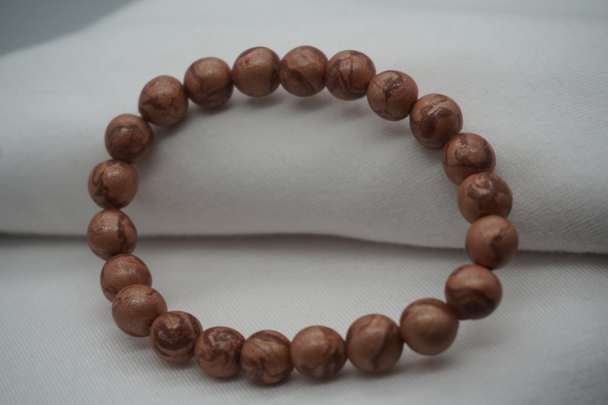 A bracelet made of copper-colored round beads against a white backdrop.  The beads sparkle and have a slight swirled pattern.