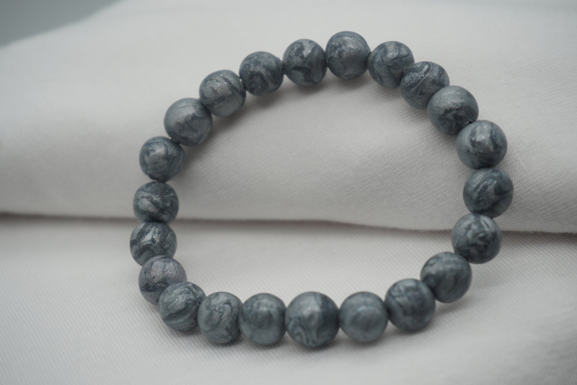 A bracelet made of silver-colored round beads against a white backdrop.  The beads sparkle and have a slight swirled pattern.