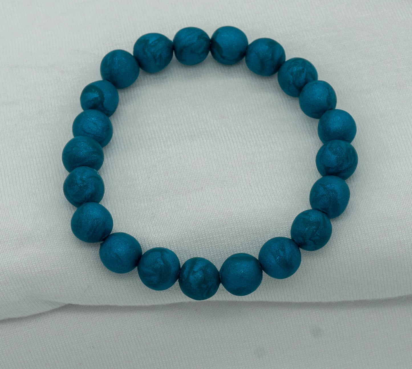 A bracelet made of teal-colored round beads against a white backdrop.  The beads sparkle and have a slight swirled pattern.