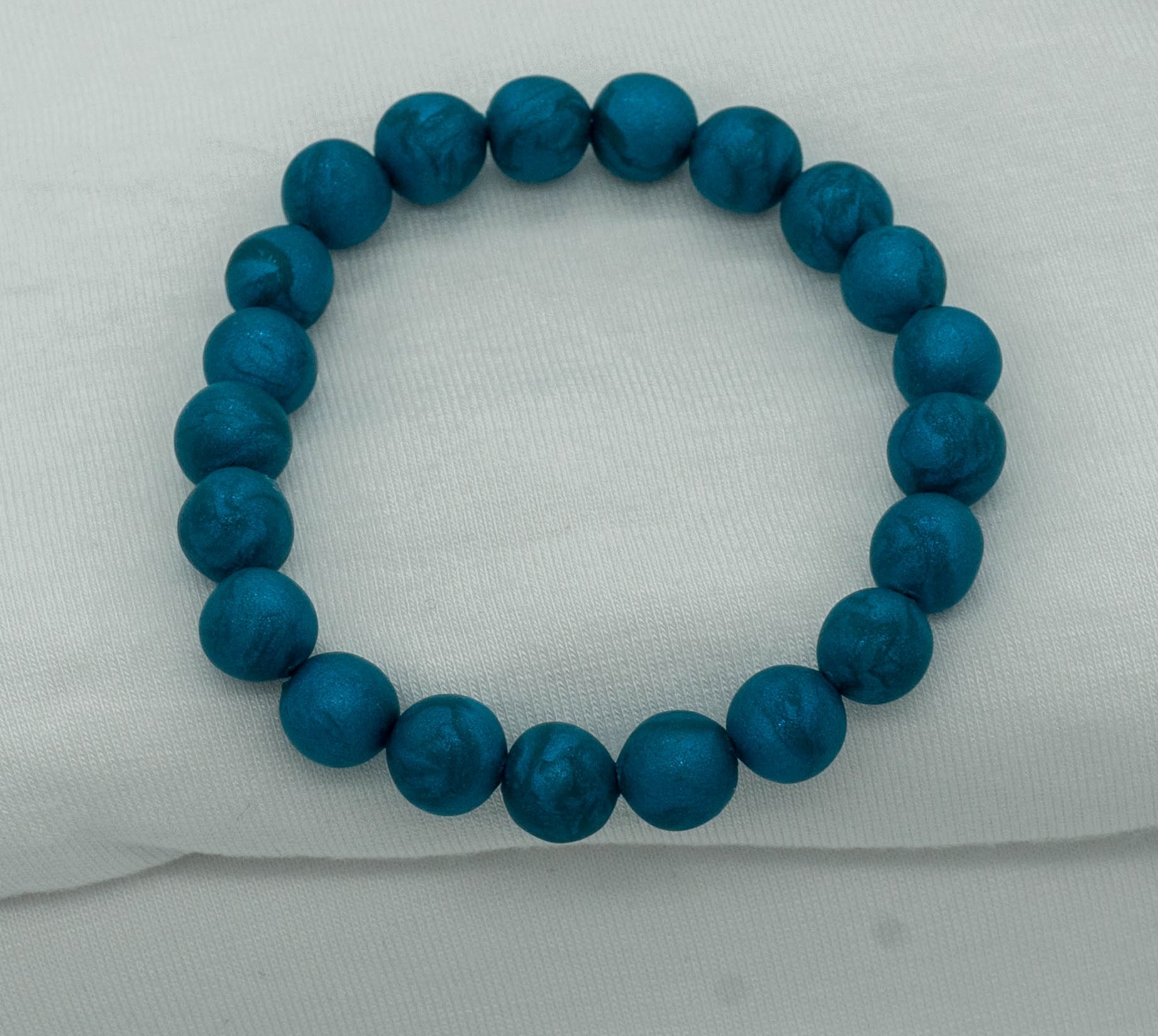 A bracelet made of teal-colored round beads against a white backdrop.  The beads sparkle and have a slight swirled pattern.
