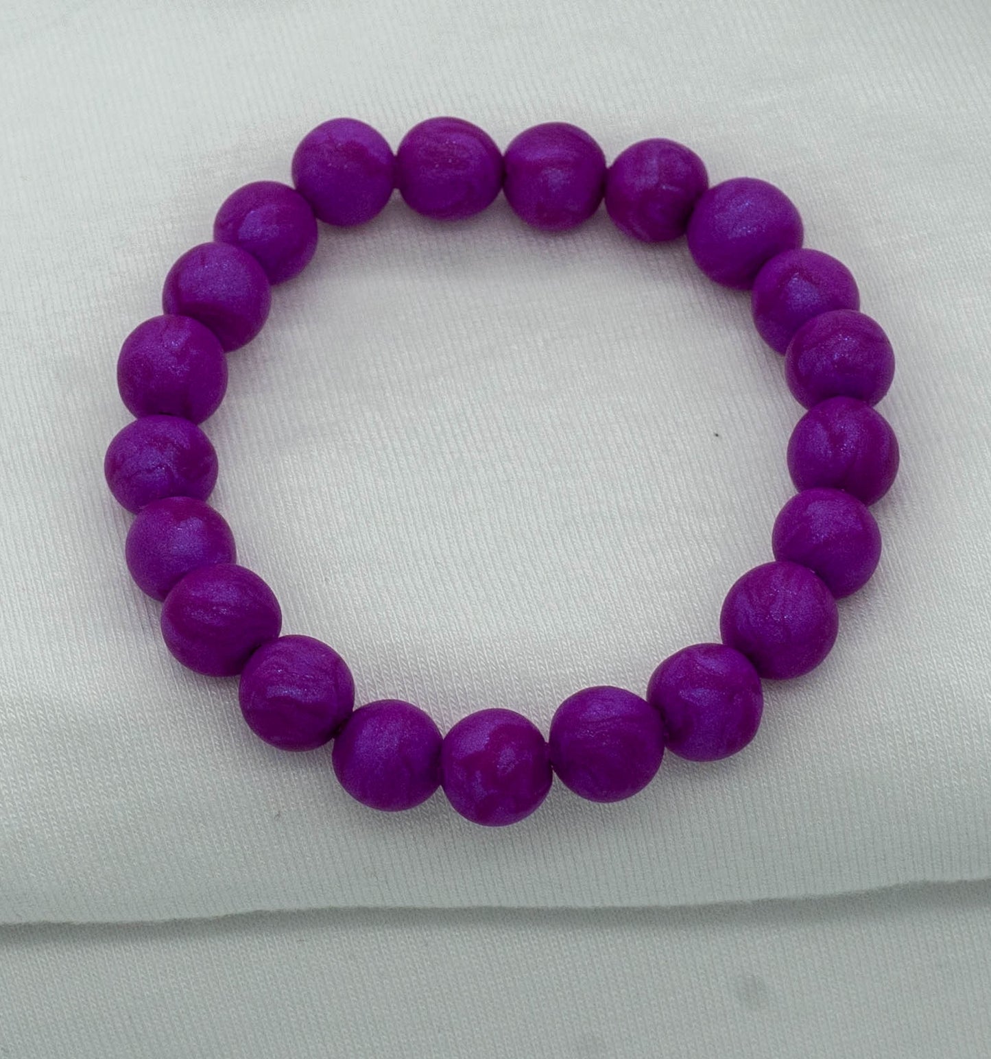 A bracelet made of purple-colored round beads against a white backdrop.  The beads sparkle and have a slight swirled pattern.