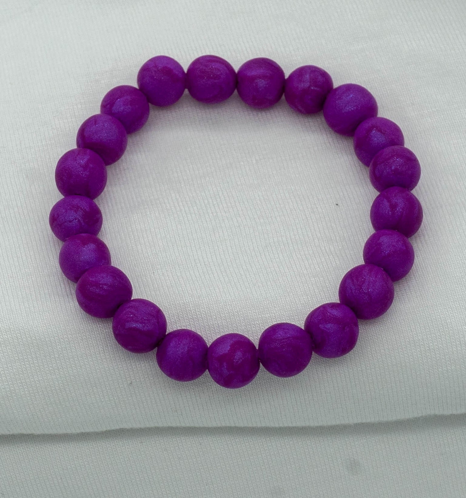 A bracelet made of purple-colored round beads against a white backdrop.  The beads sparkle and have a slight swirled pattern.